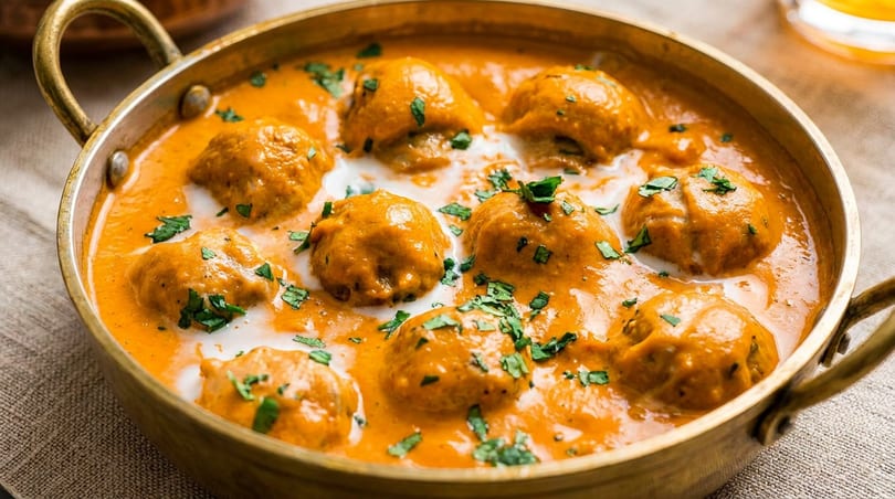 Malai Kofta, Indian cheese and vegetable dumplings in a creamy orange sauce, garnished with cilantro.