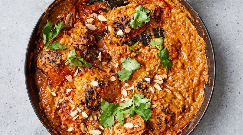 Grilled chicken in a rich orange sauce, garnished with cilantro and sliced almonds in a black pan.