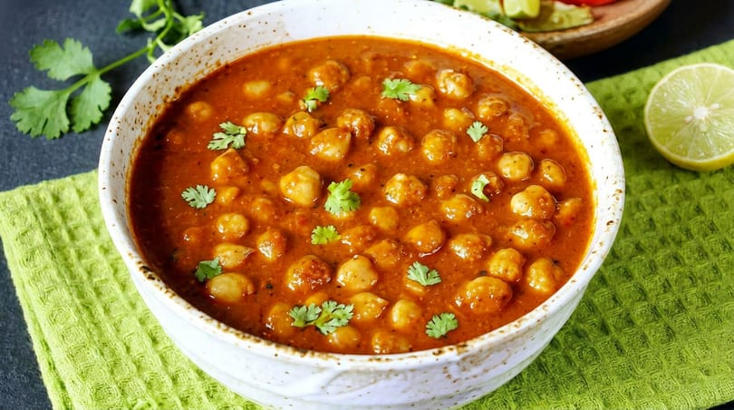 A white bowl filled with chana masala, garnished with cilantro, on a green napkin.