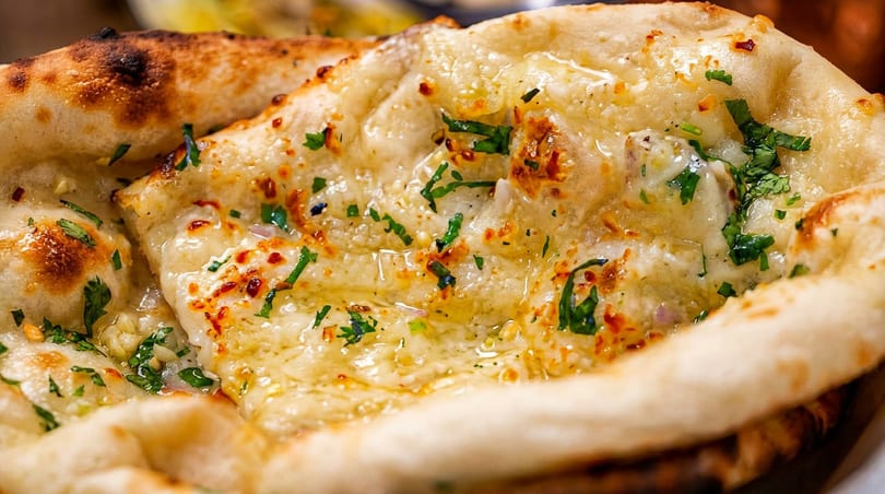 Close-up of golden-brown naan bread, glistening with butter and sprinkled with fresh green herbs.