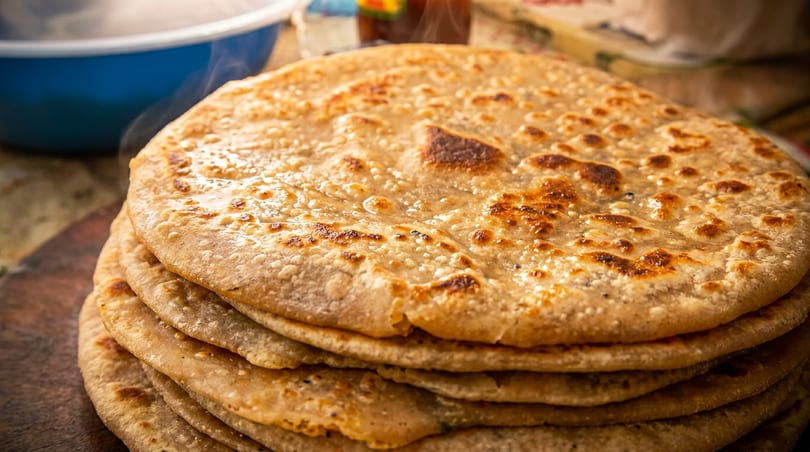 Stack of freshly made, golden-brown parathas with a blue bowl in the background.