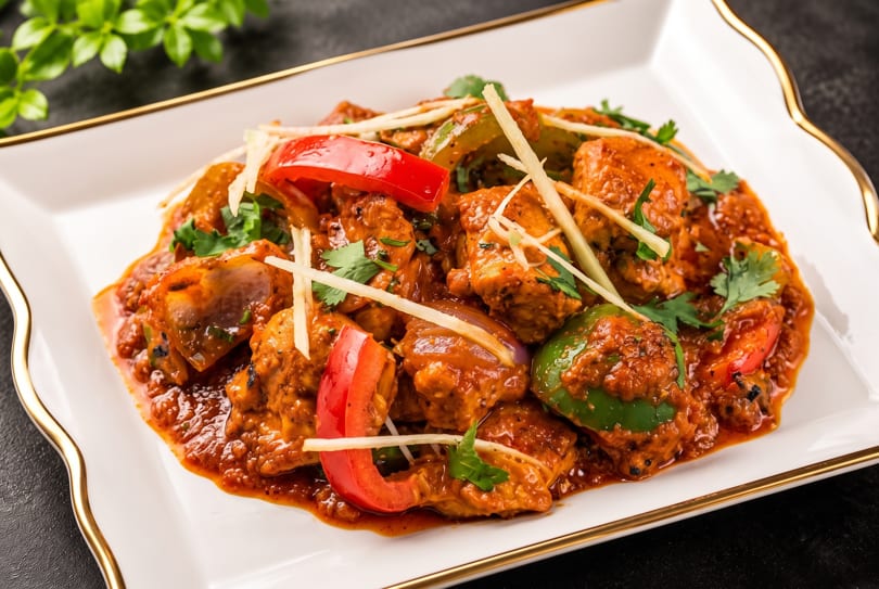 Chicken karahi with red and green bell peppers, garnished with ginger and cilantro on a white plate.